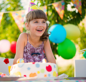 Little girl wearing a birthday hat, smiling at an outdoor birthday party
